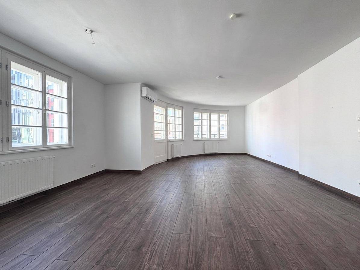 Weitläufiges, helles Zimmer mit dunklem Holzboden und mehreren Fenstern, ideal für individuelle Gestaltung.
