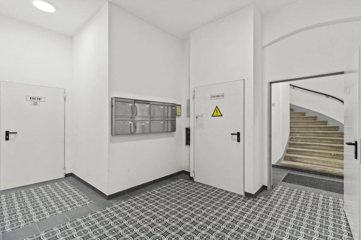 Eingangsbereich mit gemusterten Bodenfliesen, Briefkästen und Zugang zu einem Treppenhaus.