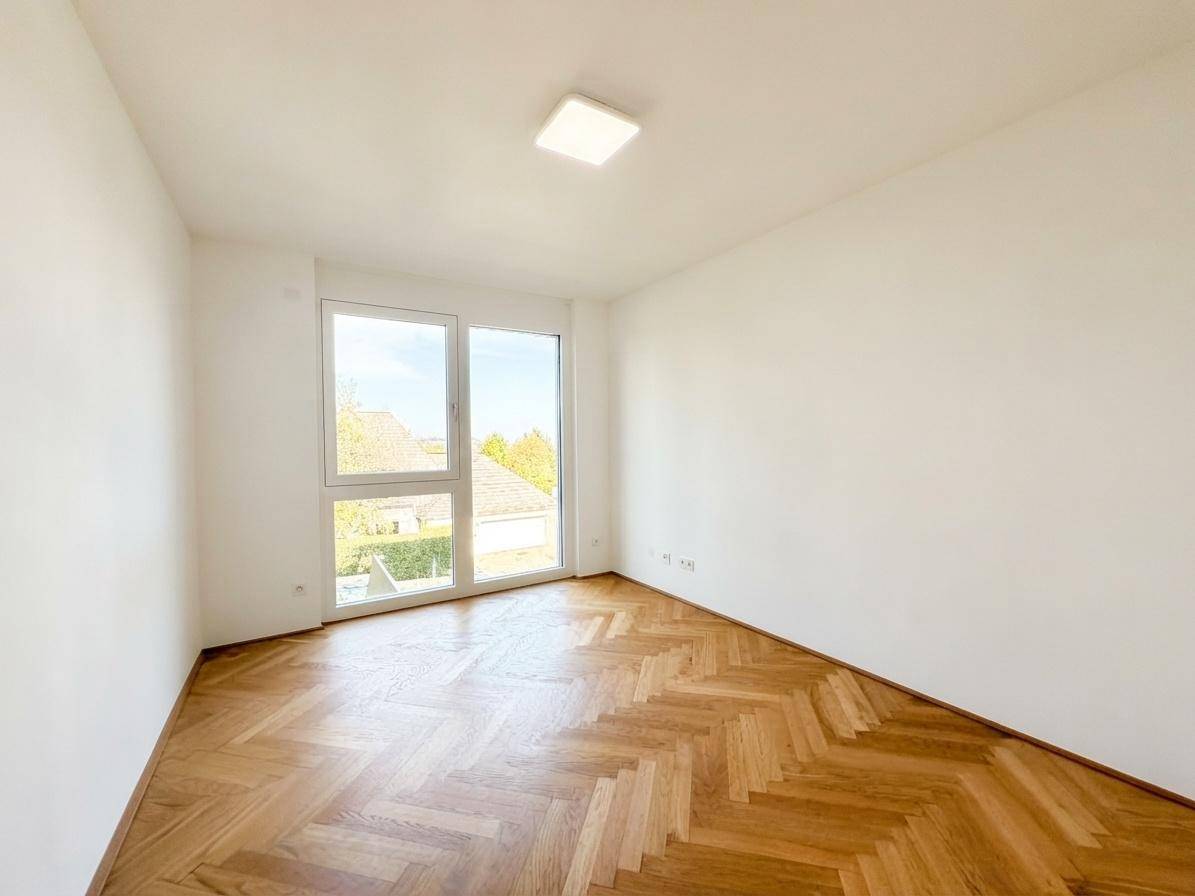 Helles Schlafzimmer mit Fischgrätparkett und großen Fenstern, die viel Tageslicht hereinlassen.