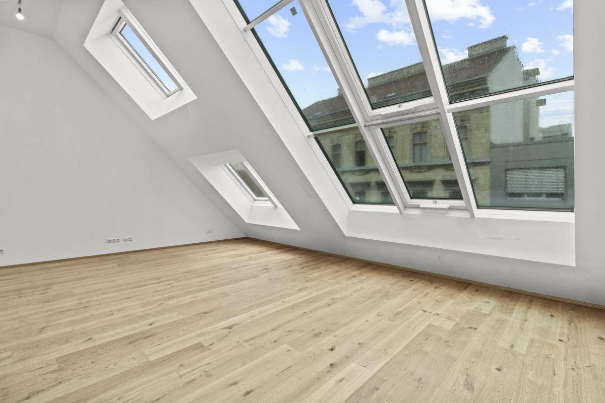 Geräumiger, heller Raum mit Holzboden und großen Dachfenstern, die einen Blick auf die Stadt bieten.