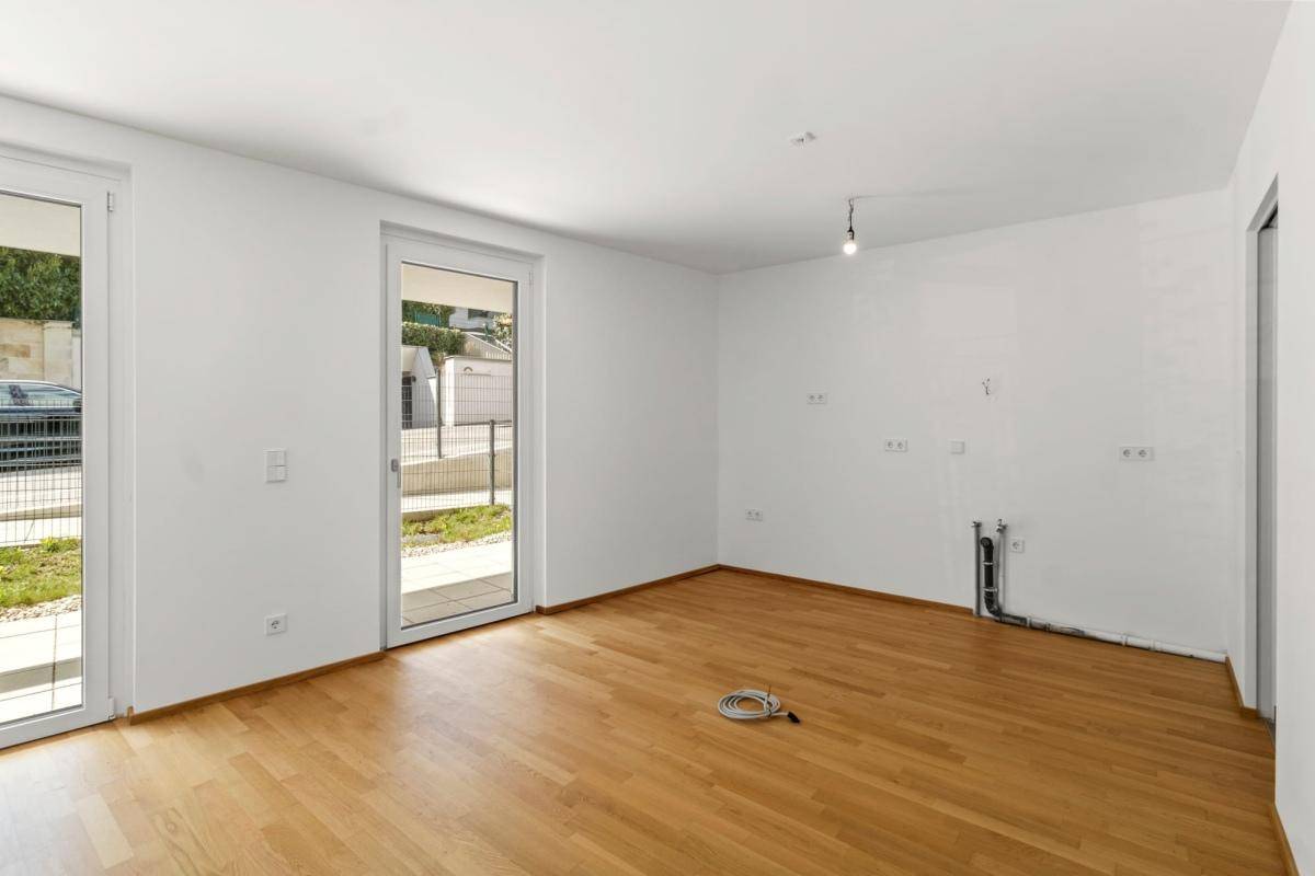 Leerer Küchenbereich mit Anschlüssen für Geräte und Zugang zur Terrasse.