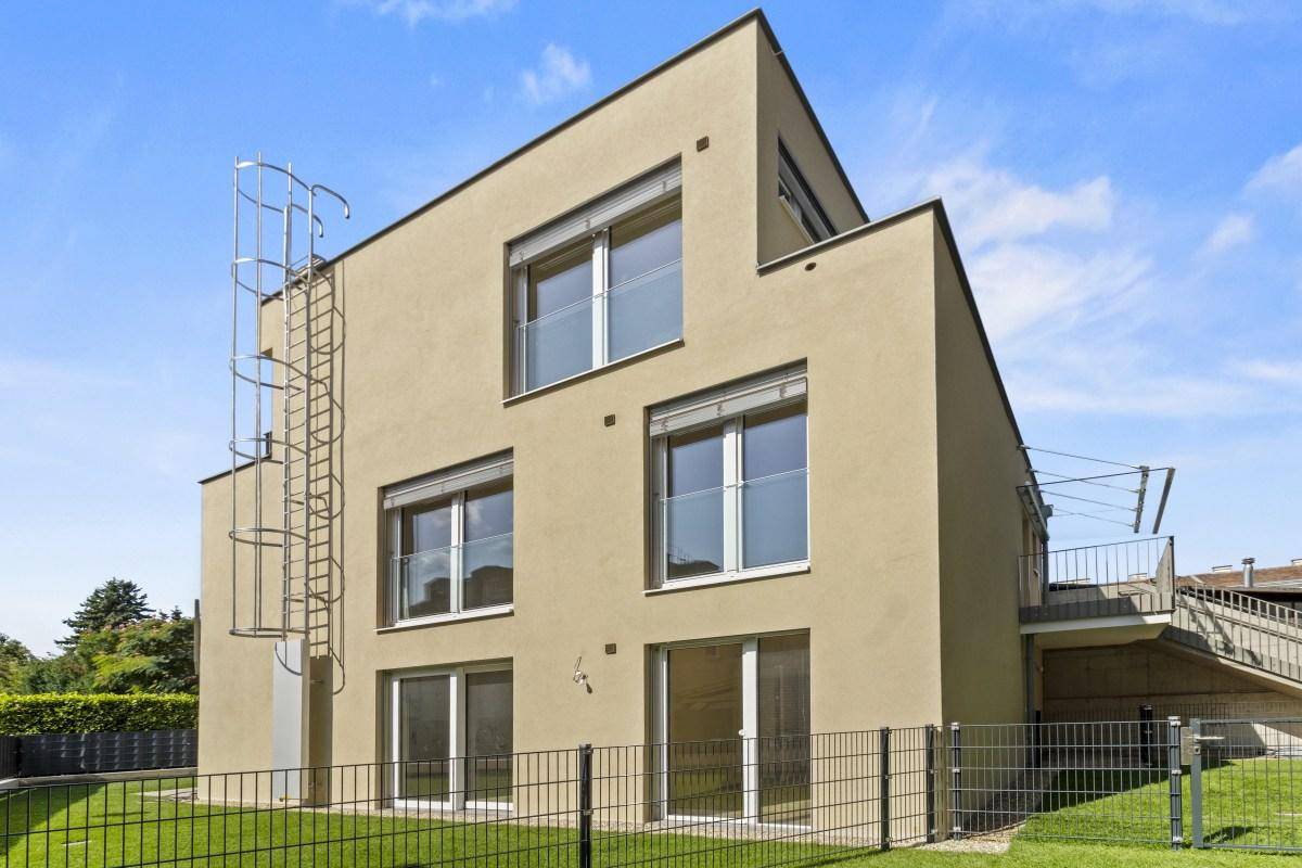 Moderne Seitenansicht des Neubaus mit großen Fenstern, Rollläden und einer außenliegenden Leiter.