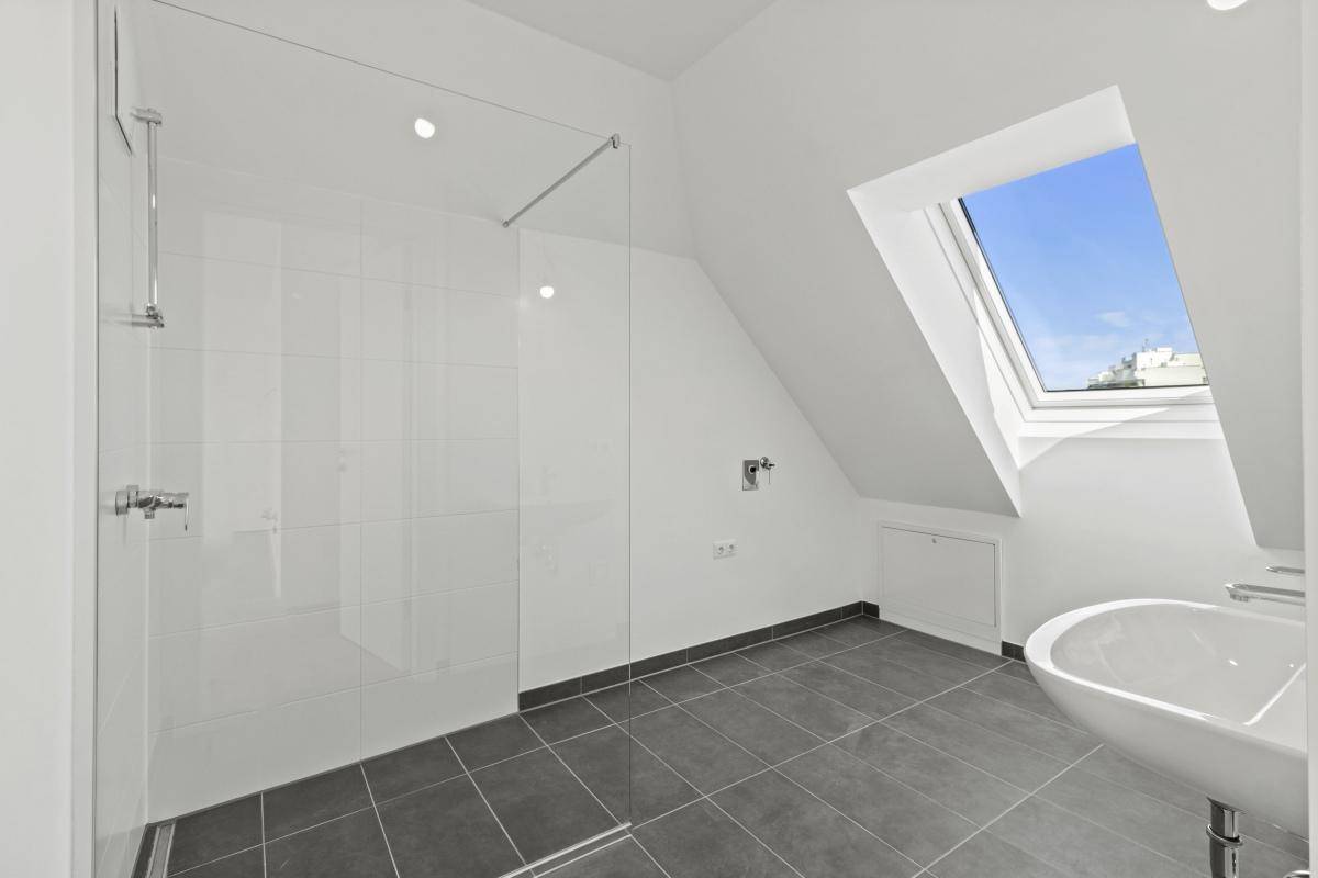 Modernes Badezimmer im Dachgeschoss mit begehbarer Dusche, Dachfenster und dunklen Fliesen.