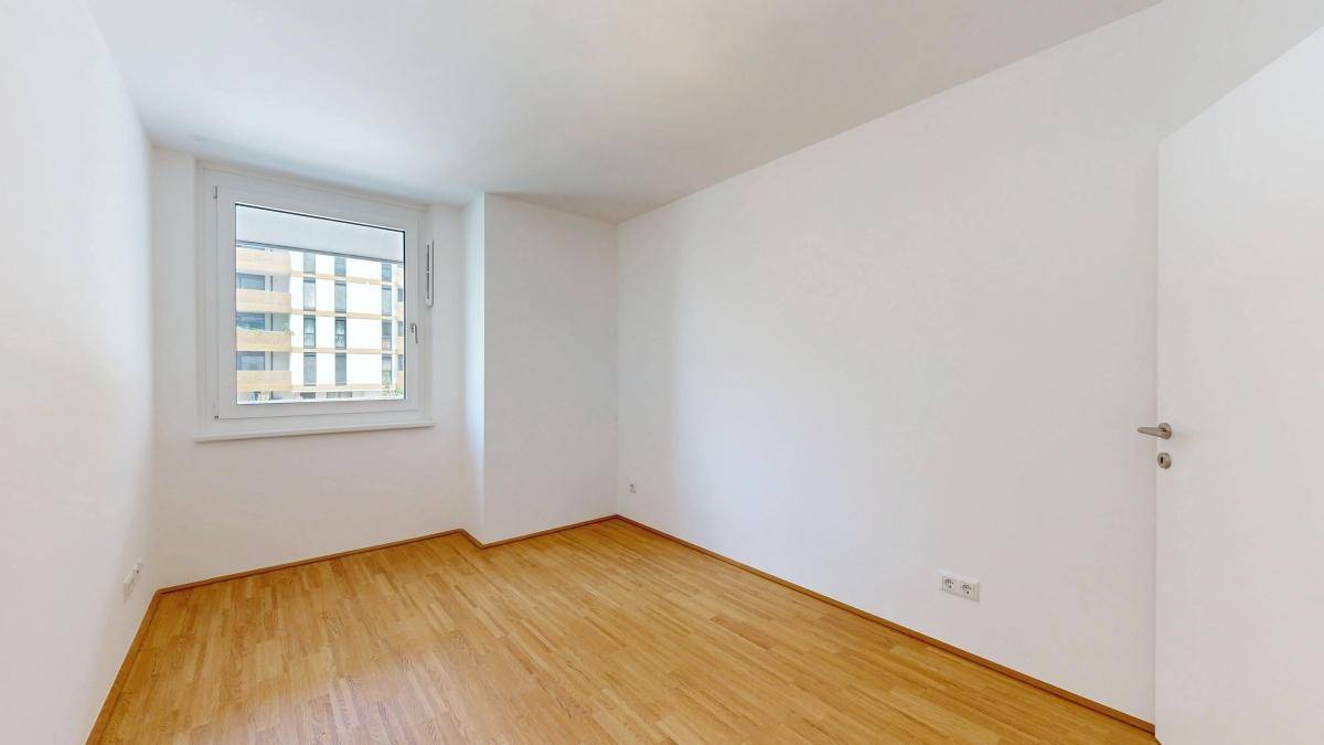 Helles Schlafzimmer mit Parkettboden und Fenster mit Blick auf die Umgebung.