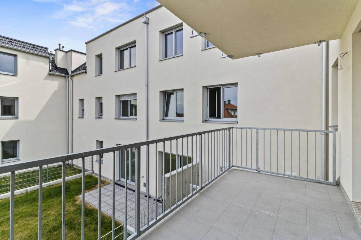 Balkon mit Fliesenboden und Blick auf den Innenhof des modernen Wohngebäudes.