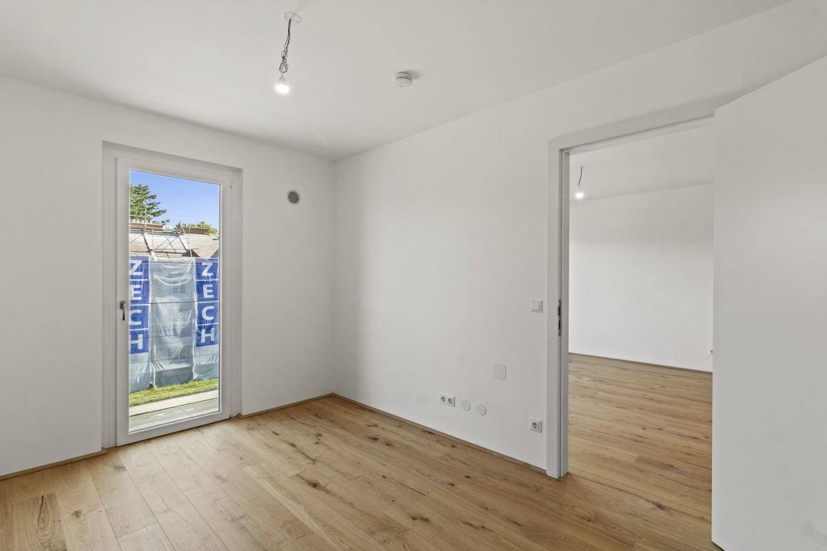 Leeres Schlafzimmer mit Holzboden und Fenster, das viel Tageslicht hereinlässt.