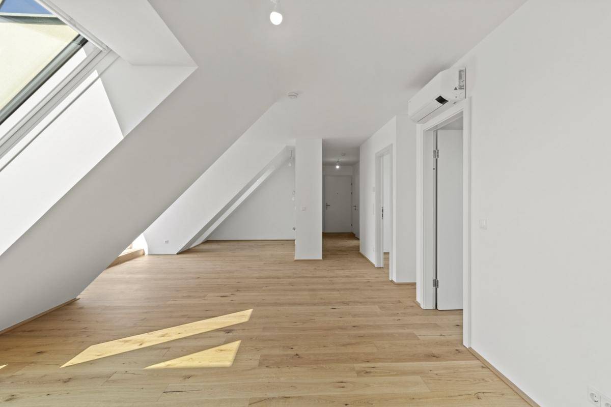 Heller Wohnraum im Dachgeschoss mit Holzboden, schrägen Wänden und großen Dachfenstern.
