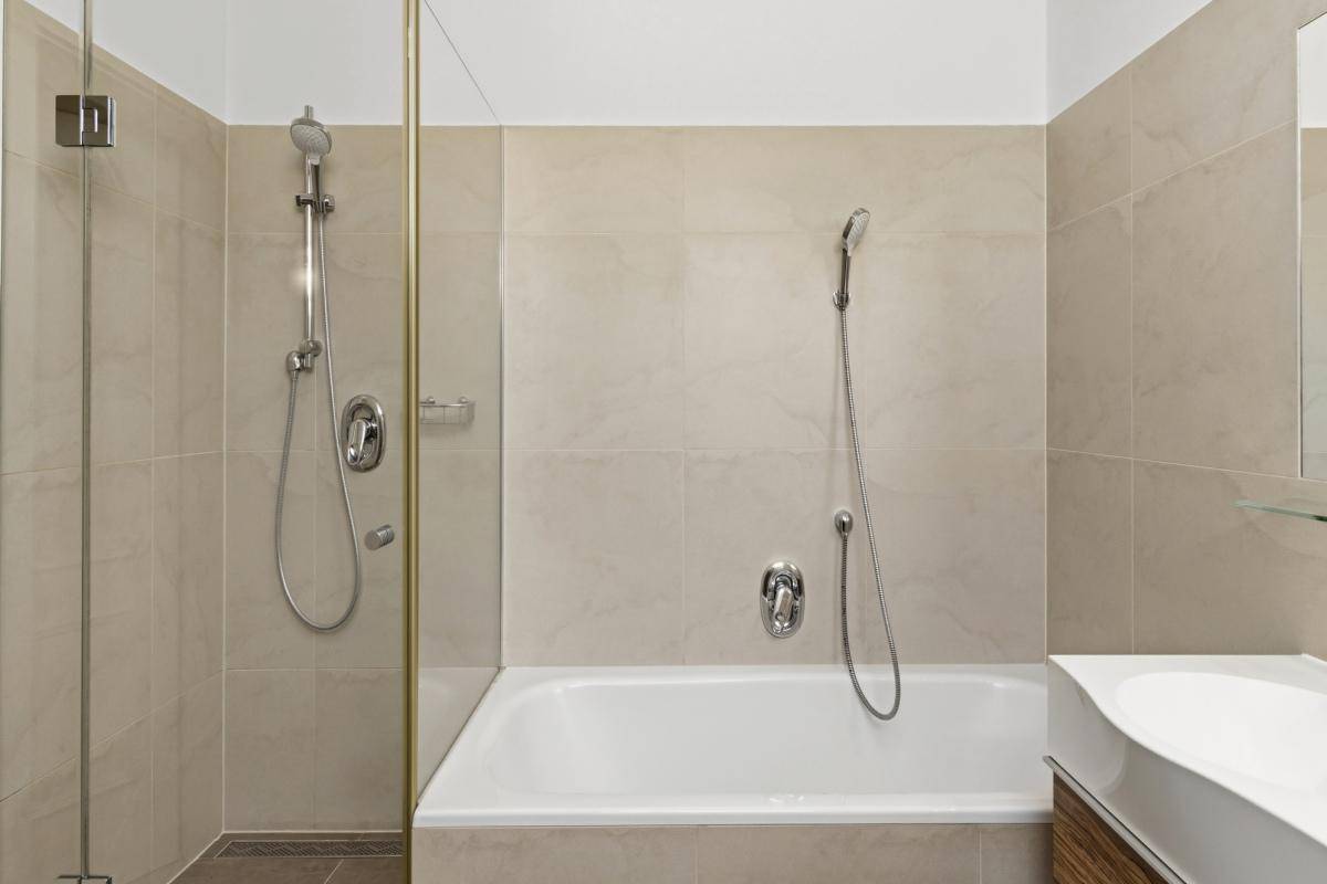 Modernes Badezimmer mit beigefarbenen Fliesen, Badewanne und separatem Duschbereich.