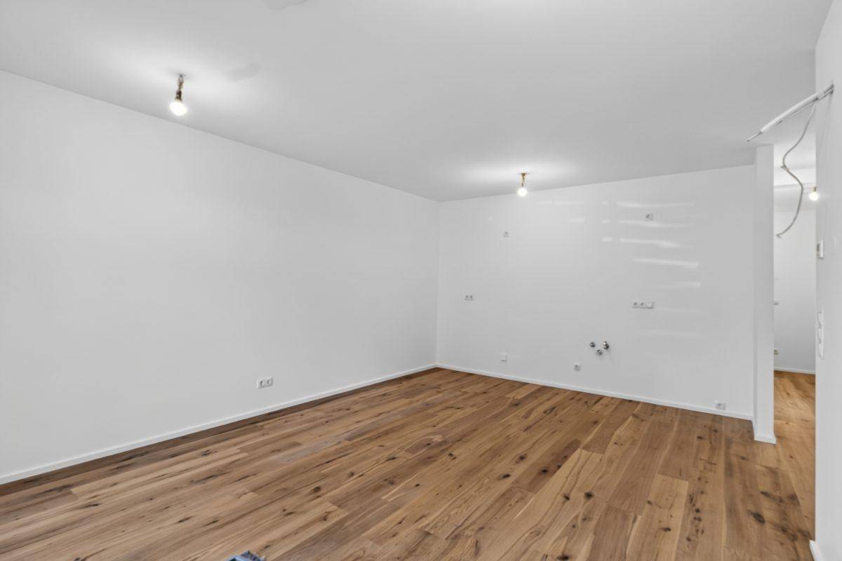 Heller Wohnraum mit Holzboden und Anschlüssen für eine offene Küche.