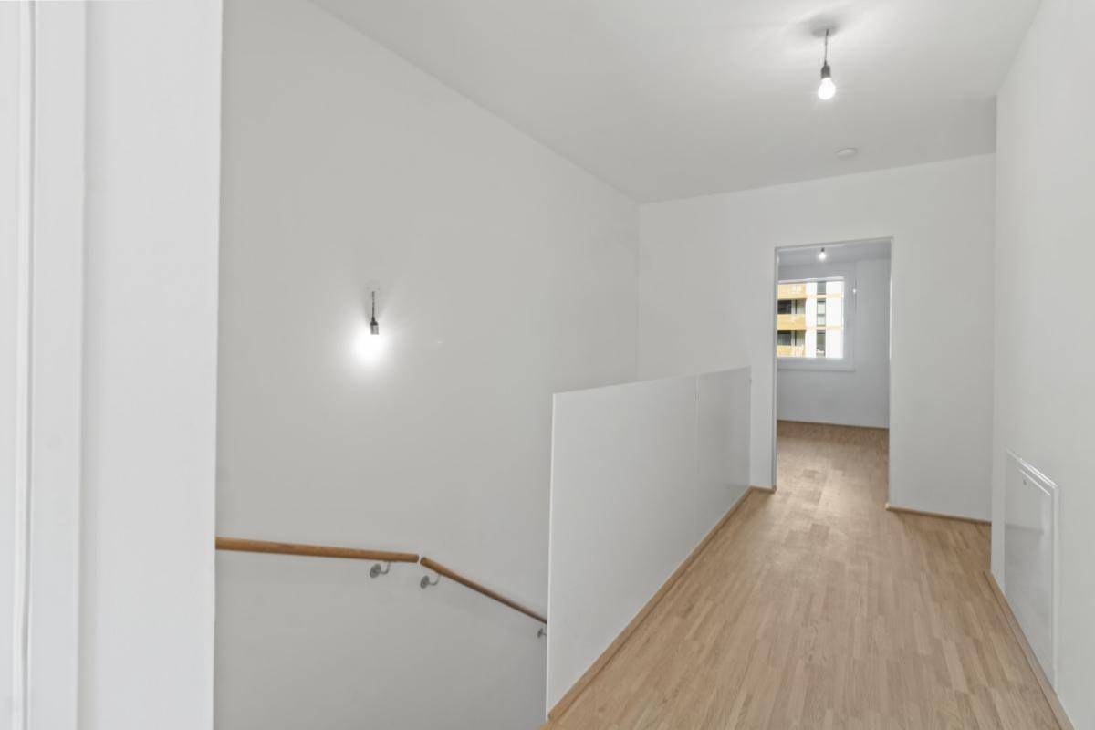 Heller Flur mit Holzboden und Treppenaufgang, der zu den oberen Etagen führt.
