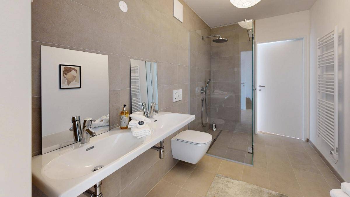 Helles Badezimmer mit großem Waschbecken, Spiegeln und ebenerdiger Dusche.