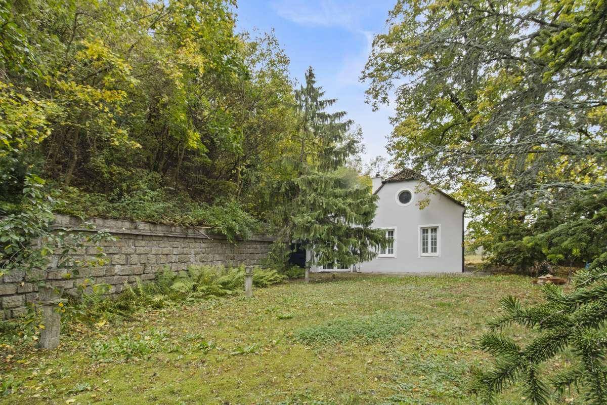 Seitenansicht des Hauses mit Rundfenster, alter Steinmauer und Garten.