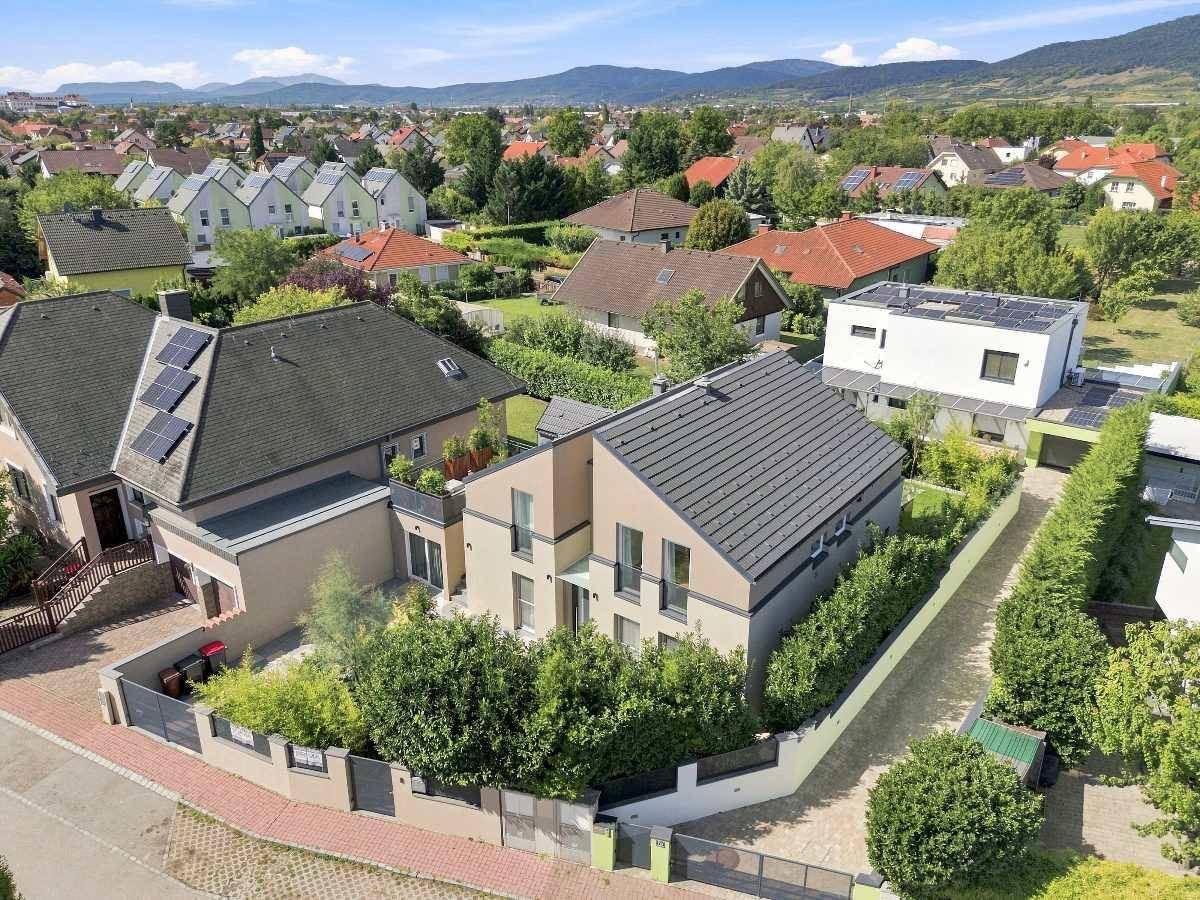 Luftaufnahme eines modernen Wohnhauses mit Solaranlage und gepflegtem Garten in grüner Umgebung.