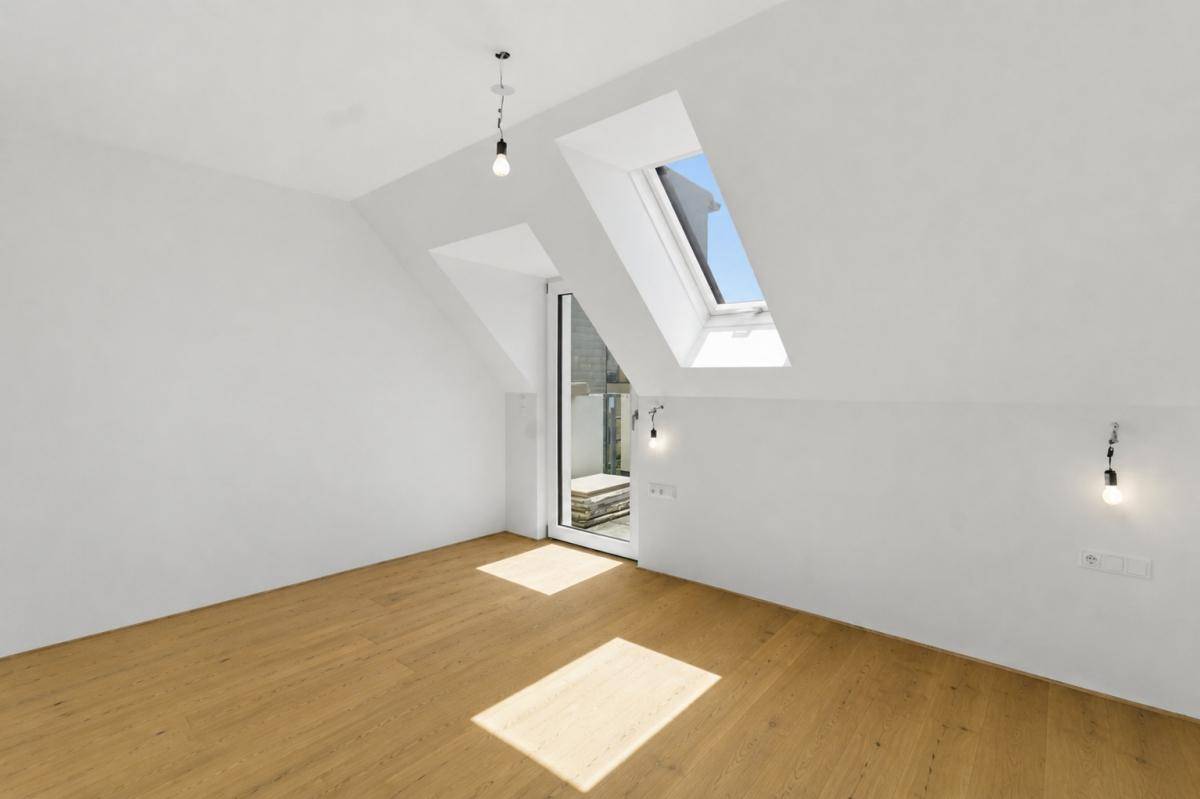 Heller Dachgeschossraum mit Holzboden, schrägen Wänden, Dachfenster und Zugang zu einem Außenbereich.