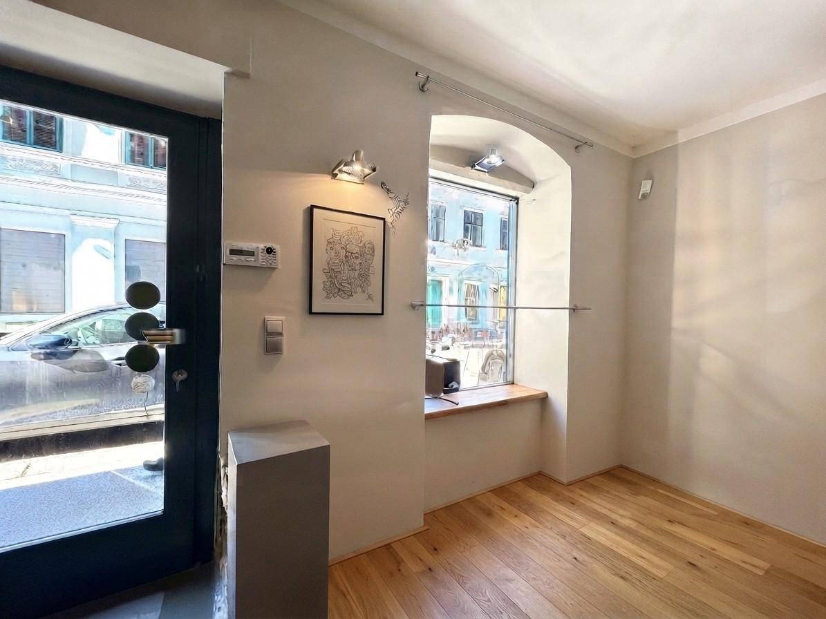Heller Innenraum eines Geschäfts mit Holzdielenboden, einem großen Fenster zur Straße und einer modernen Eingangstür.