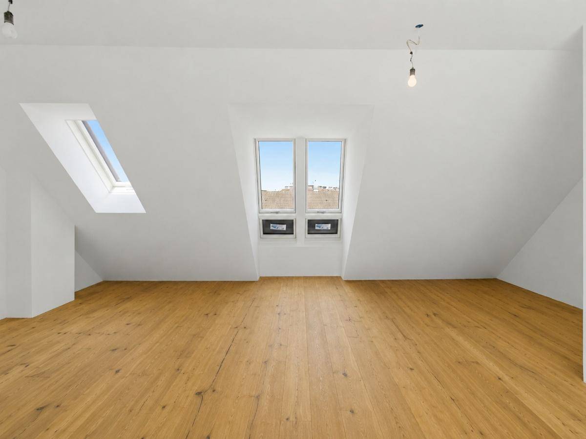 Geräumiger, leerer Dachgeschossraum mit Holzboden und zwei vertikalen Fenstern in der Schräge.