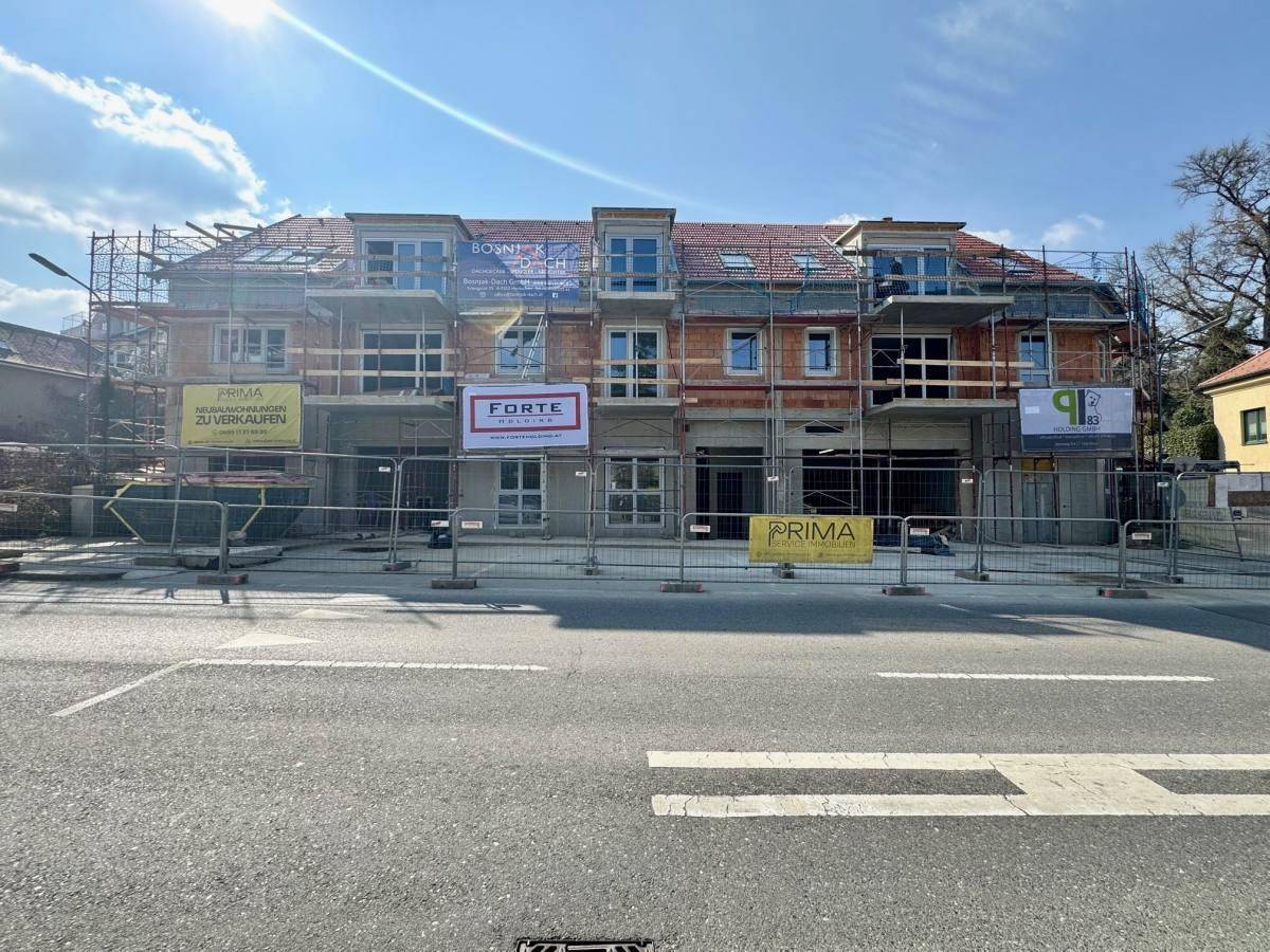 Vorderansicht der Baustelle eines Neubauprojekts mit Gerüst und Werbebannern.