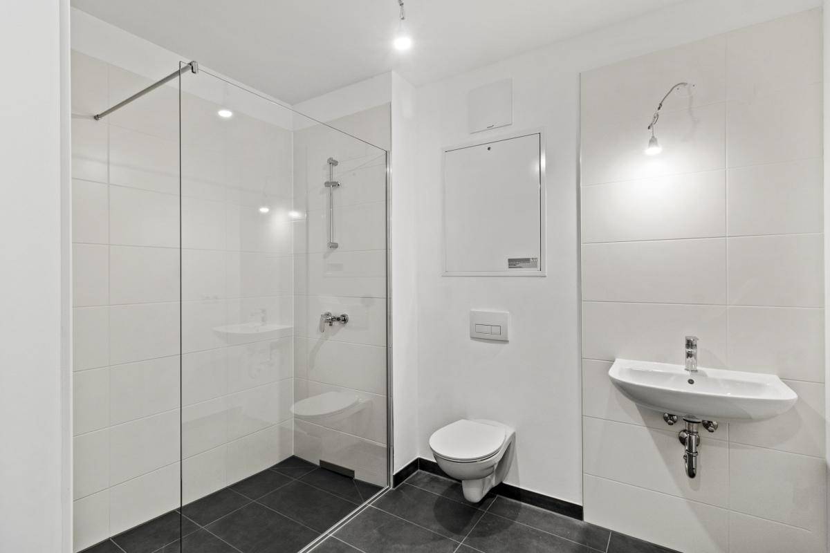Modernes Badezimmer mit weiß gefliesten Wänden, dunklem Boden und begehbarer Dusche.