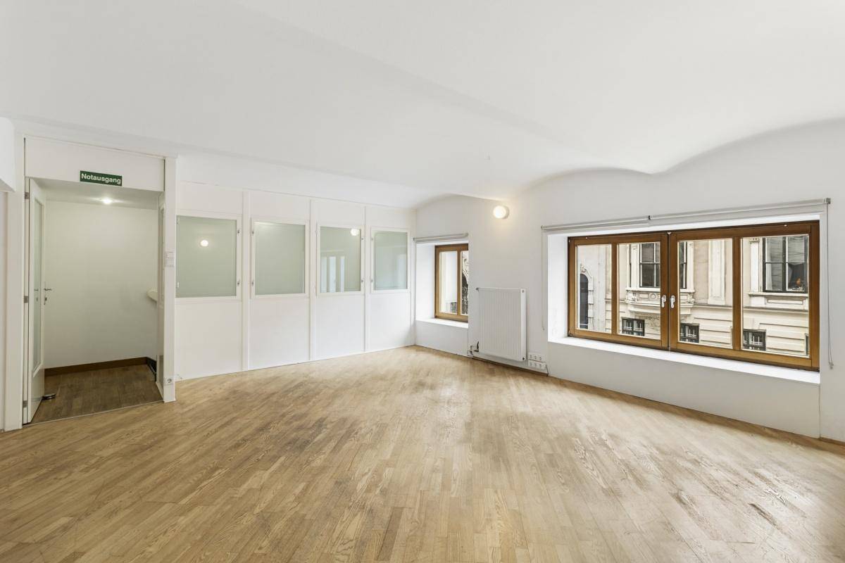 Geräumiger Bürobereich mit Holzboden, weißen Wänden und Fenstern, die viel Tageslicht hereinlassen, einladende Atmosphäre.