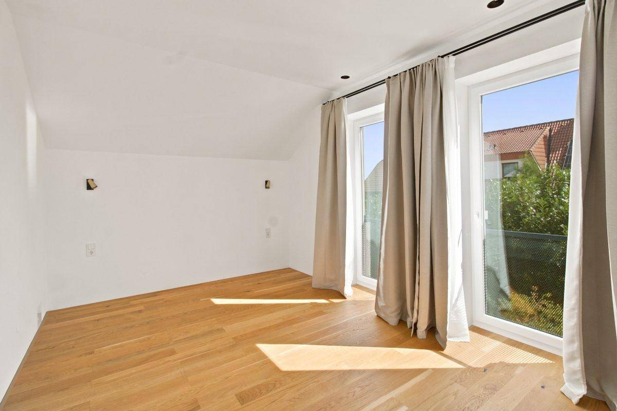 Helles Schlafzimmer mit Holzboden, großen Fenstern und Blick auf die Umgebung.