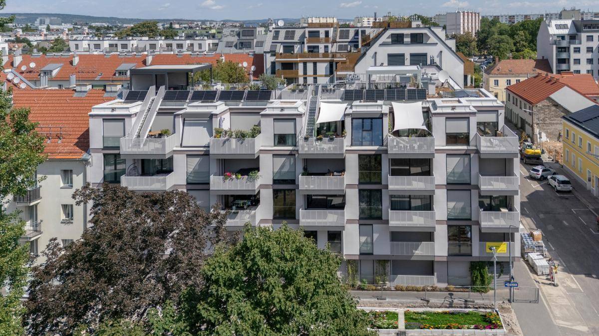 Luftaufnahme eines modernen Wohngebäudes mit Balkonen und Dachterrassen in städtischer Umgebung.