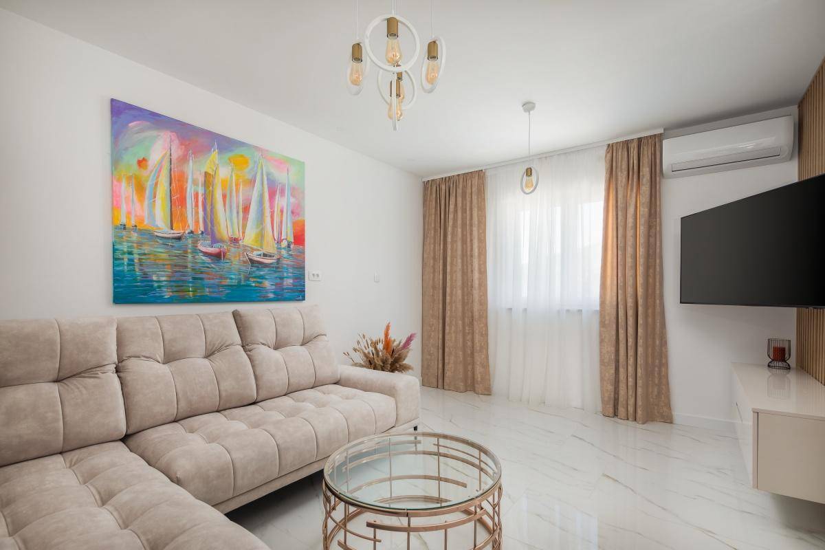 Gemütliches Wohnzimmer mit beigem Sofa, modernem Kunstwerk und hellem Fliesenboden.