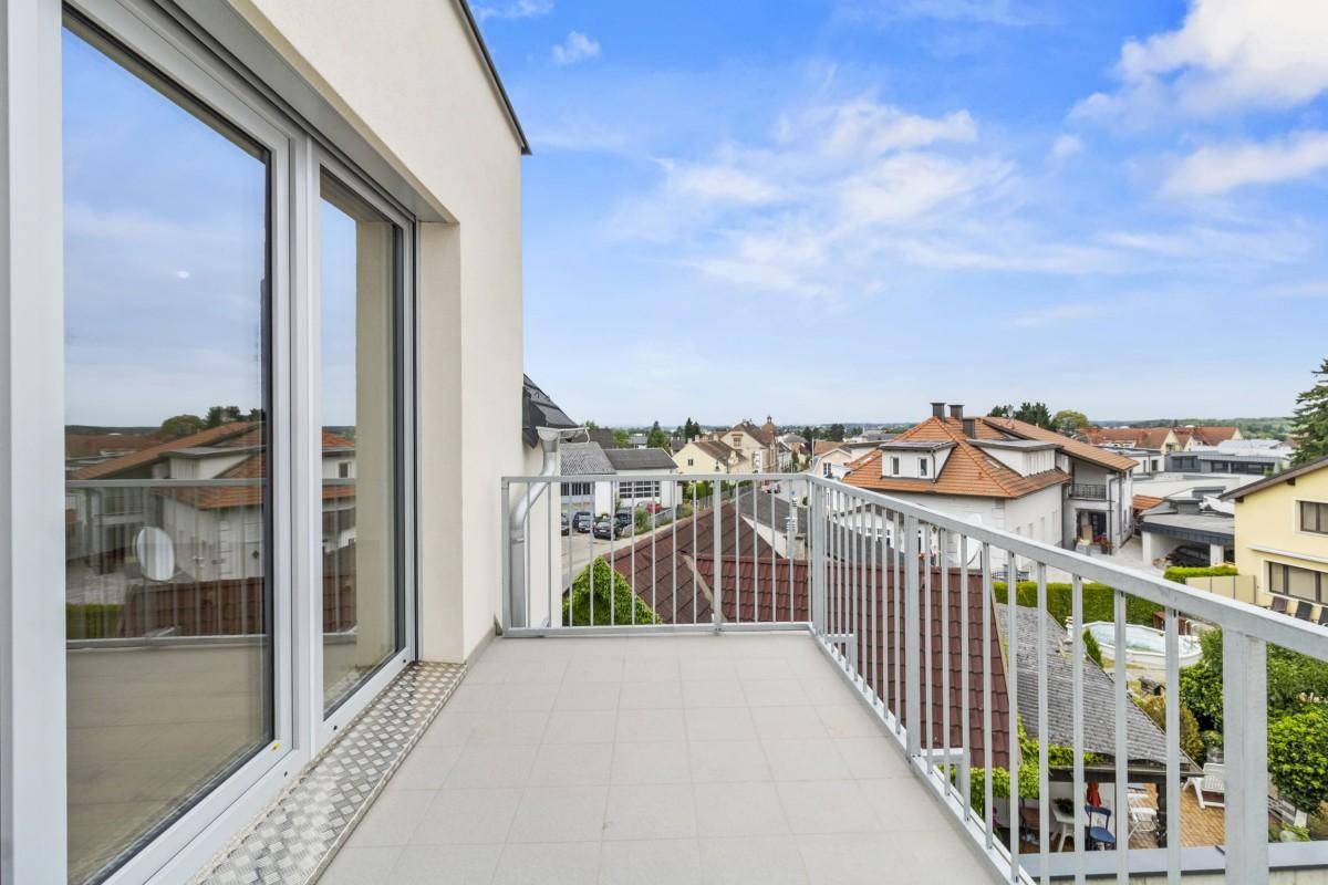 Heller Balkon mit Fliesenboden und Blick auf die umliegende Wohnbebauung und den Himmel.