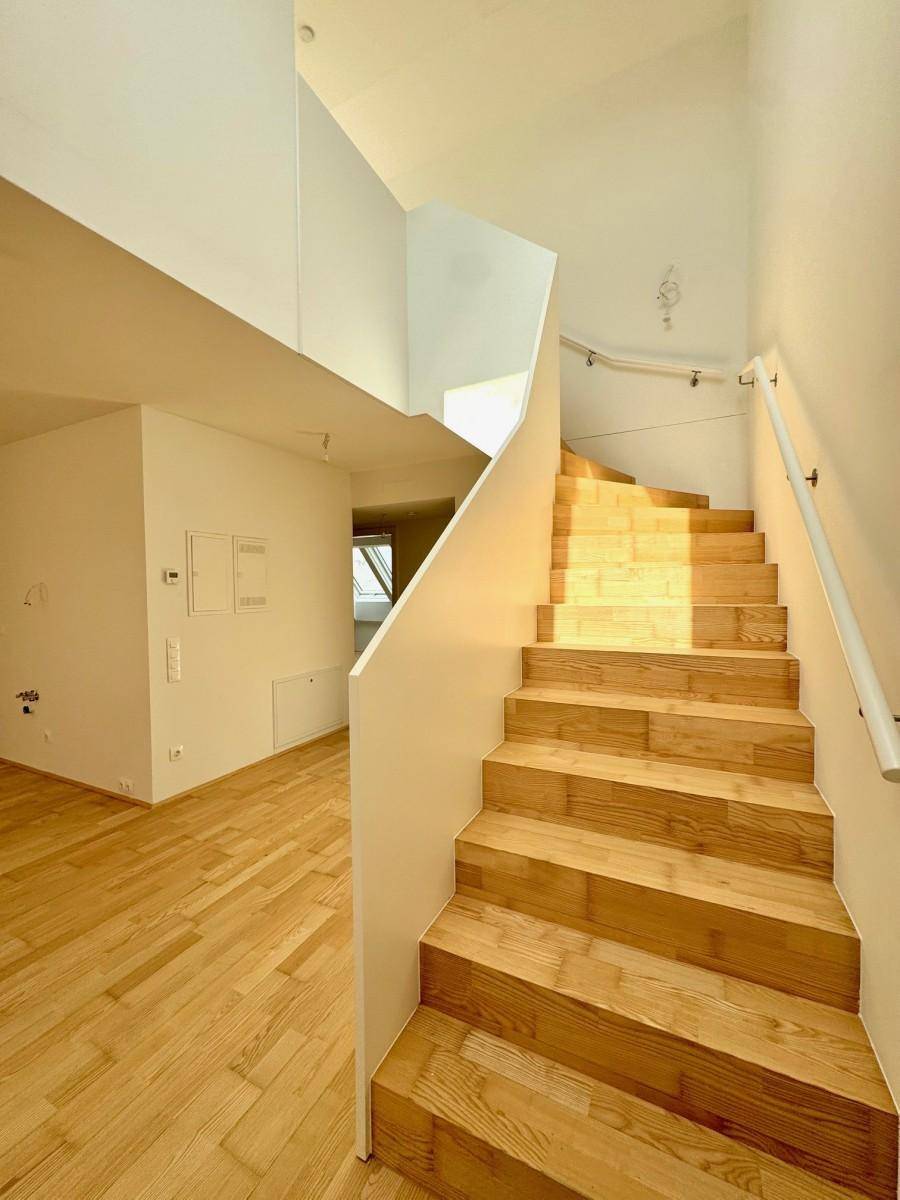 Helle Holztreppe mit modernem Geländer, die in die obere Etage führt, gut beleuchtet.