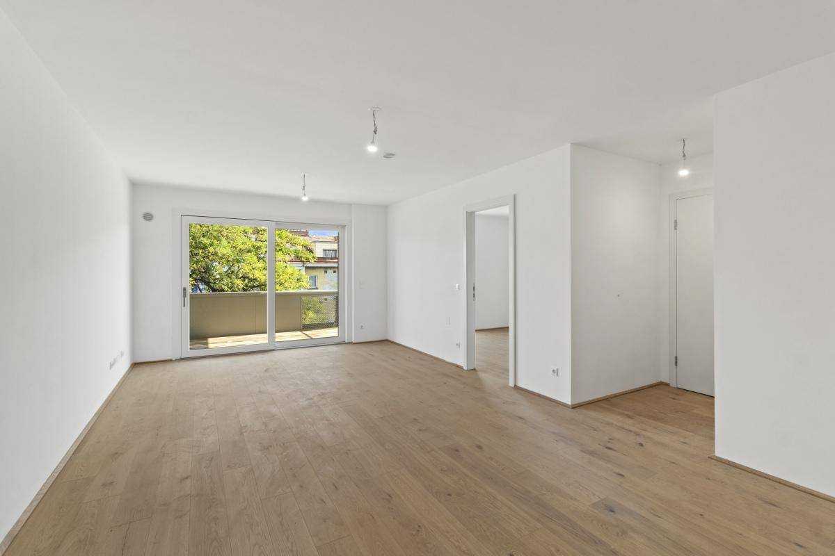 Helles Wohnzimmer mit Holzboden, Balkonzugang und Blick in einen angrenzenden Raum.