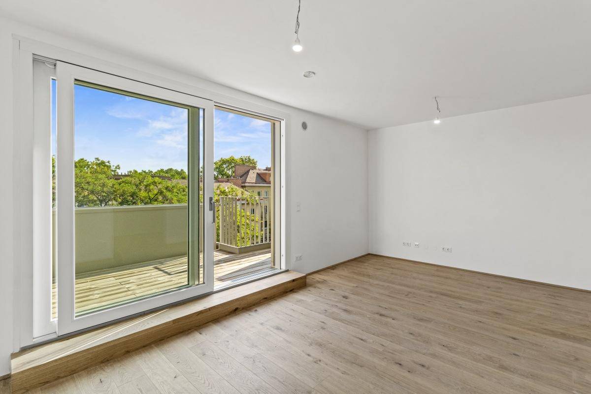 Leerer Raum mit Holzboden und großen Schiebetüren, die zu einem Balkon führen.