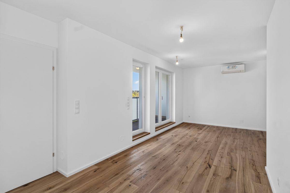 Geräumiger Wohnbereich mit Holzboden, Klimaanlage und Zugang zu einem französischen Balkon.