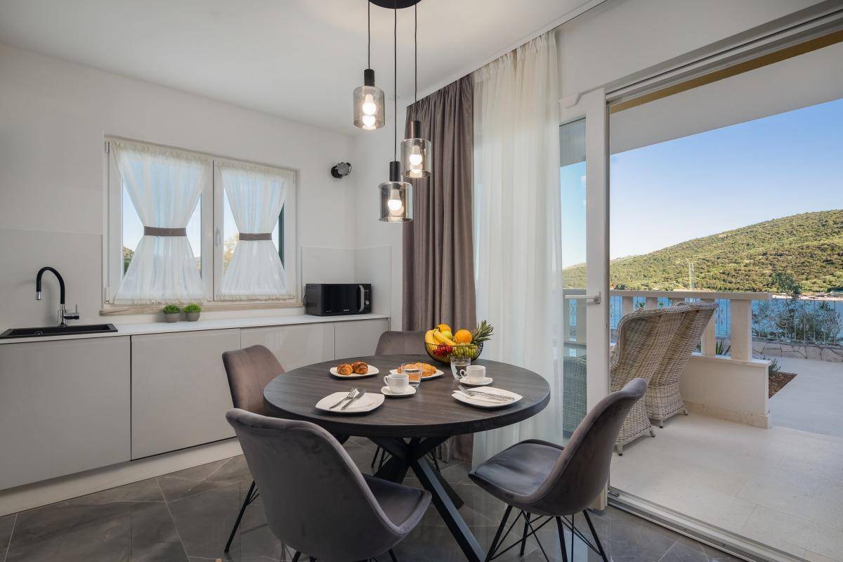 Moderne Küche mit Essbereich, Balkonzugang und Blick auf die grüne Landschaft und das Meer.