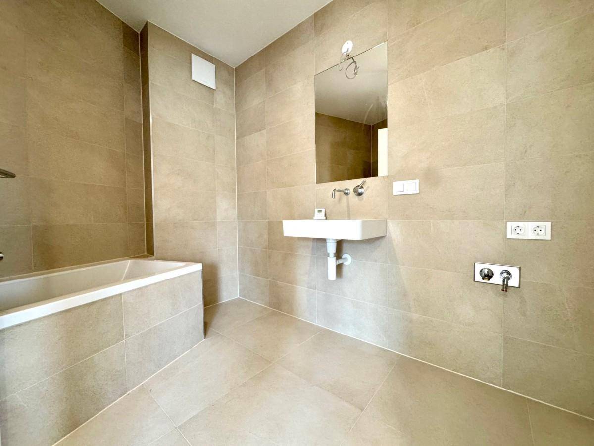 Modernes Badezimmer mit beigefarbenen Fliesen, Badewanne und Waschbecken.