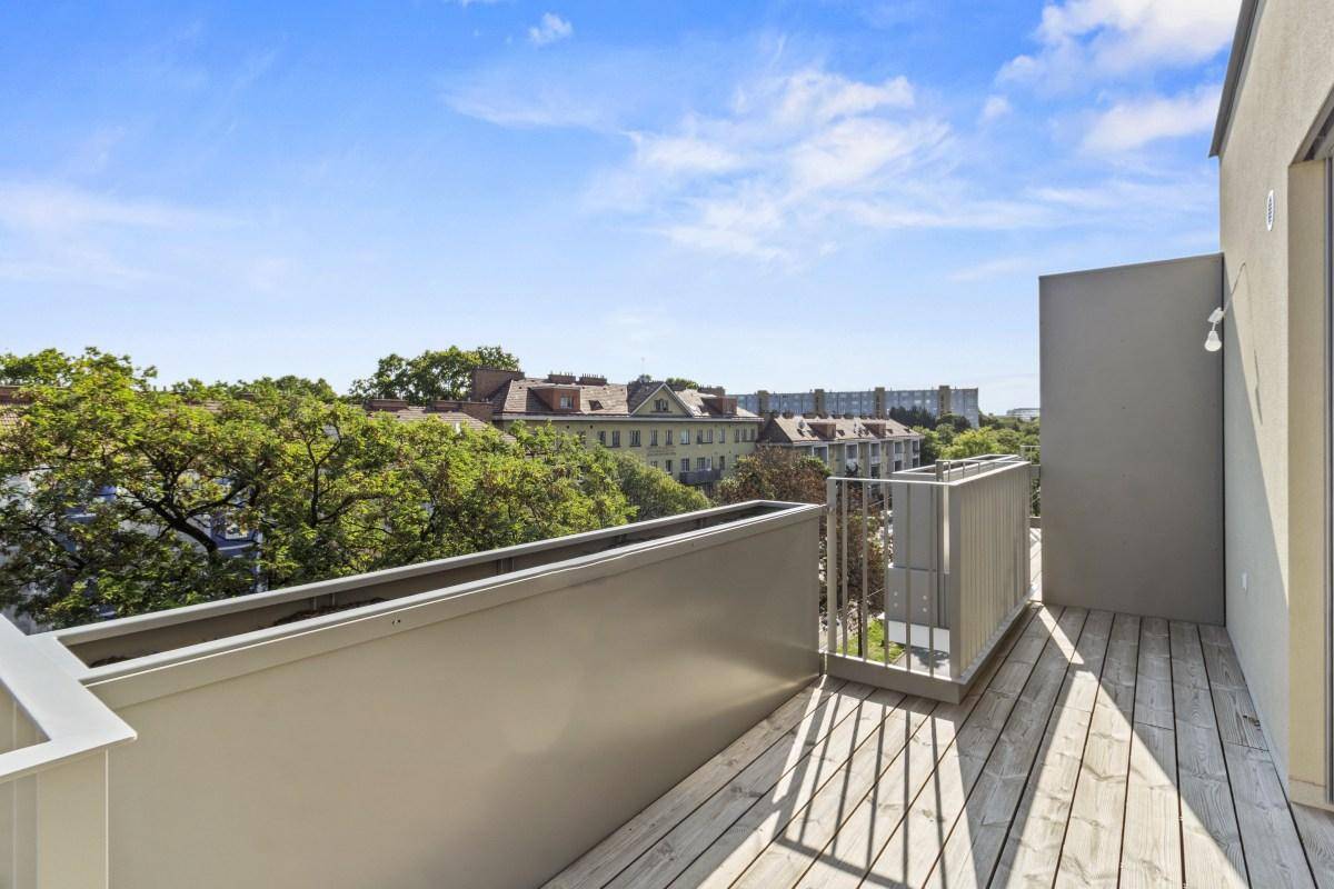 Heller Balkon mit Holzbelag und weitem Blick über die umliegende Bebauung und Bäume.