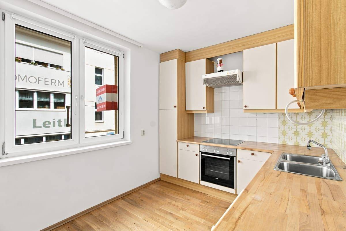 Helle Küche mit Fenster, Holzarbeitsplatte und integrierten Geräten, inklusive Waschmaschine.