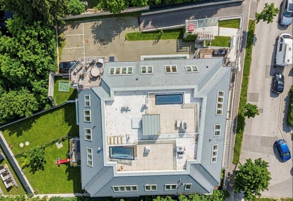 Luftaufnahme eines modernen Gebäudes mit komplexer Dachstruktur, Dachpools und umliegenden Grünflächen.