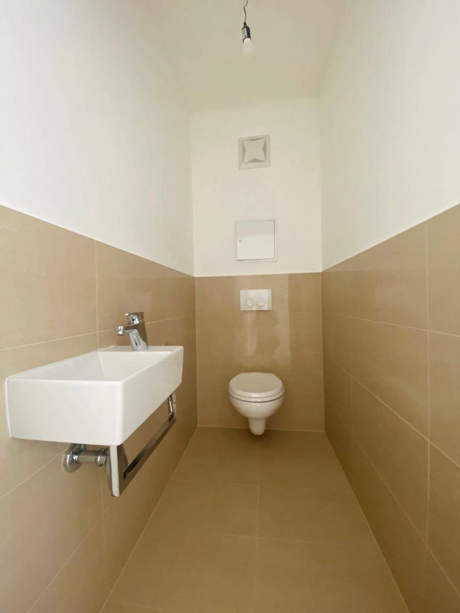 Separates Gäste-WC mit Wand-WC, Waschbecken und beigefarbenen Fliesen.