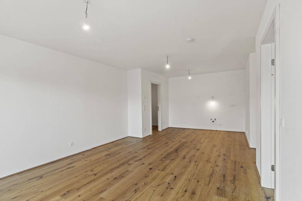 Leerer Küchenbereich mit Holzboden und vorbereiteten Anschlüssen für eine Einbauküche.