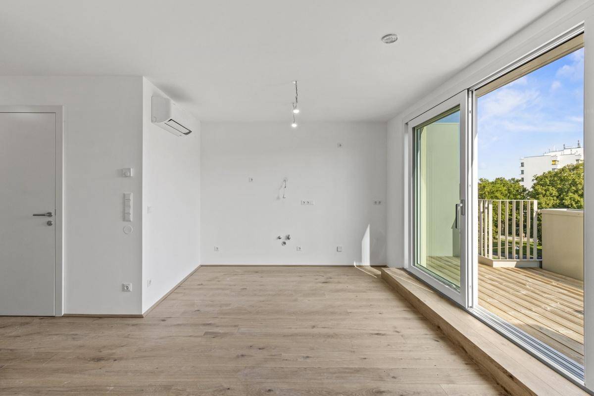 Unmöblierter Raum mit Holzboden, Klimaanlage und Zugang zu einem sonnigen Balkon.