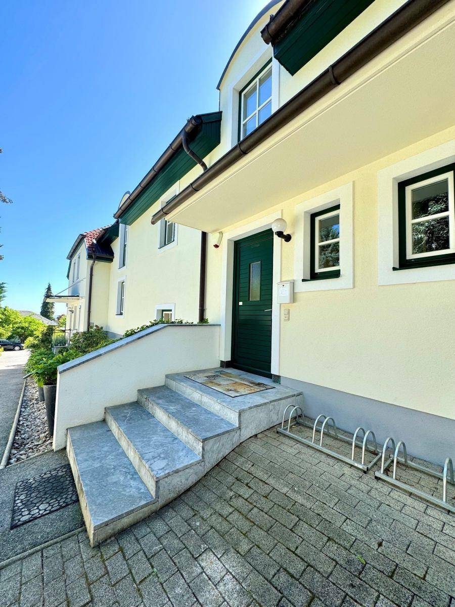 Eingangsbereich des Hauses mit Steintreppe, grüner Haustür und Fahrradständern unter strahlendem Himmel.