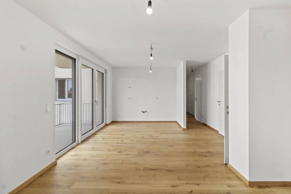 Heller Wohnbereich mit Parkettboden und Zugang zu einem Flur und Balkon.