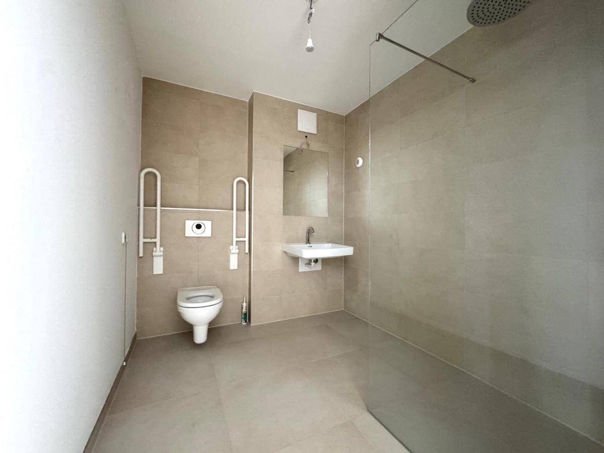Barrierefreies Badezimmer mit ebenerdiger Dusche, wandhängender Toilette und Haltegriffen.