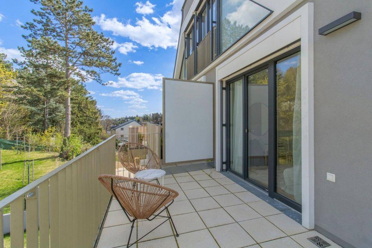 Heller Balkon mit Blick ins Grüne und auf die moderne Architektur des Gebäudes.