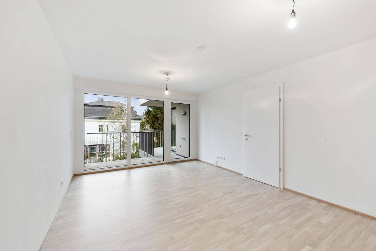 Heller, leerer Wohnraum mit hellem Parkettboden und großen Fenstern zum Balkon.