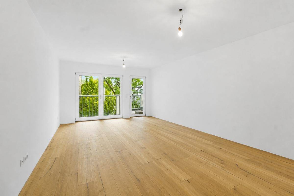 Heller Raum mit Eichenparkettboden und Zugang zu einem französischen Balkon mit Blick ins Grüne.