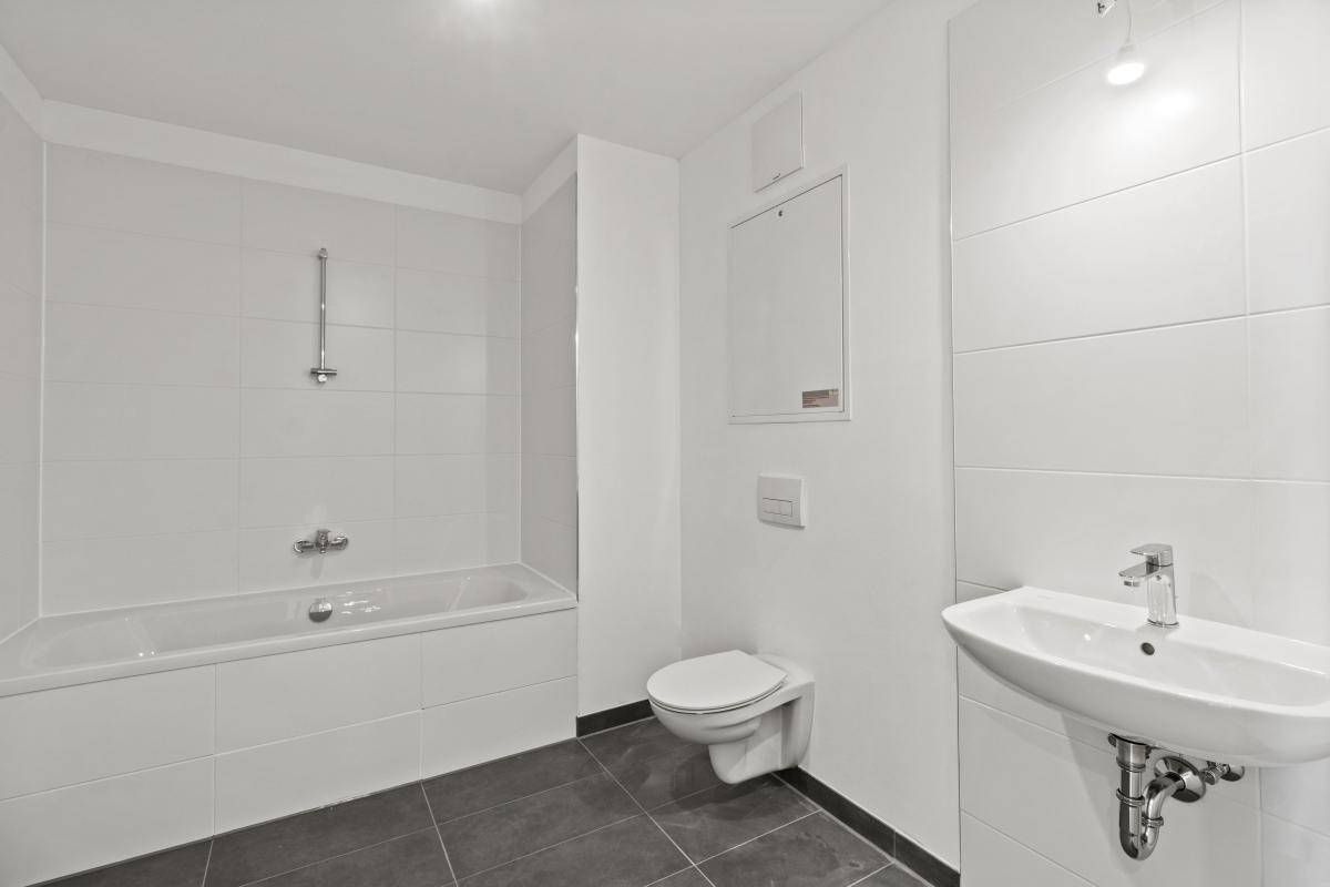 Modernes Badezimmer mit weißen Fliesen, Badewanne, WC und Einzelwaschbecken.