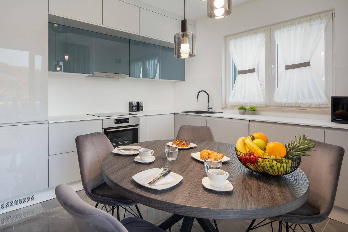 Helle, moderne Küche mit integrierten Geräten, Essbereich und Fenster mit Blick ins Grüne.