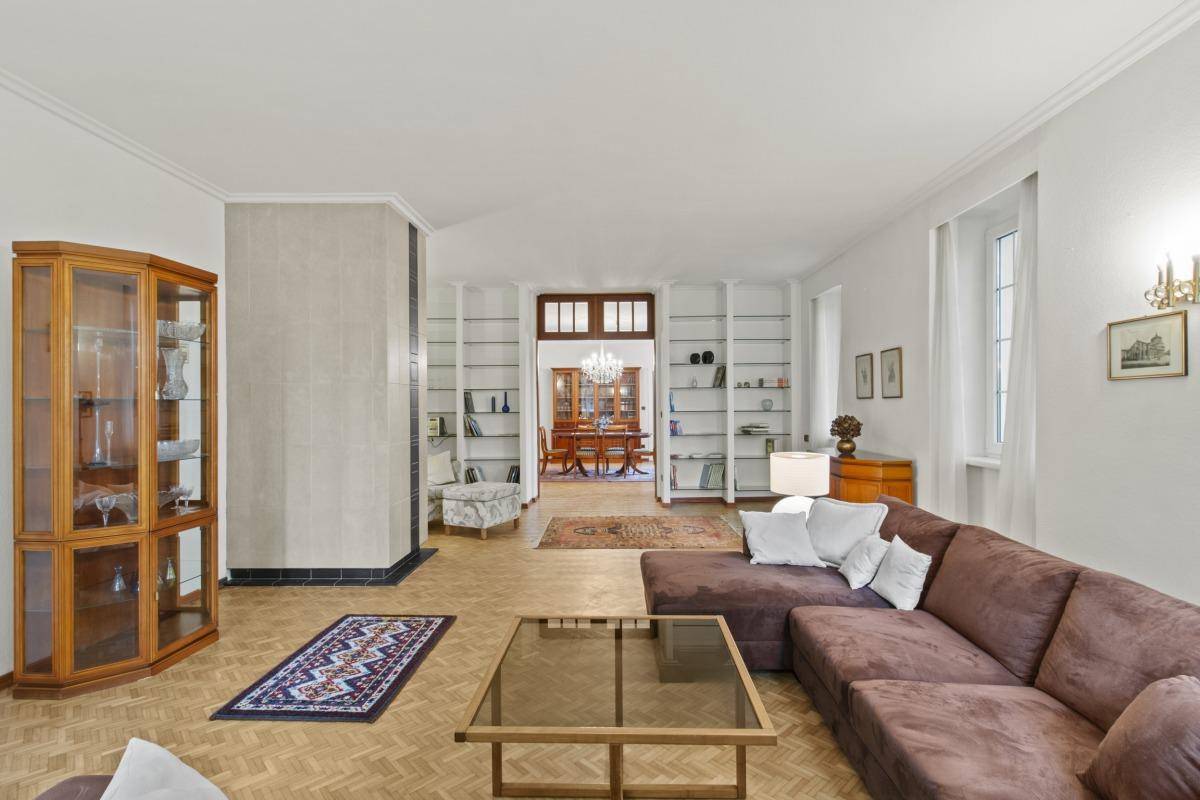 Geräumiges Wohnzimmer mit Parkettboden, Vitrine und offenem Zugang zum eleganten Esszimmer.