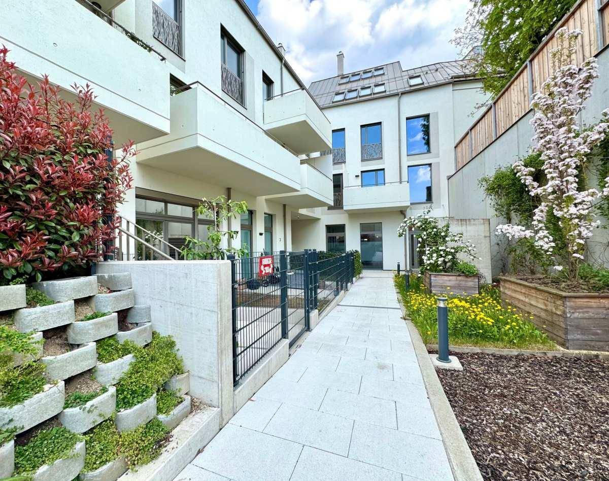 Moderner Zugangsbereich zu einem Wohngebäude mit gepflegten Grünflächen und Treppen.