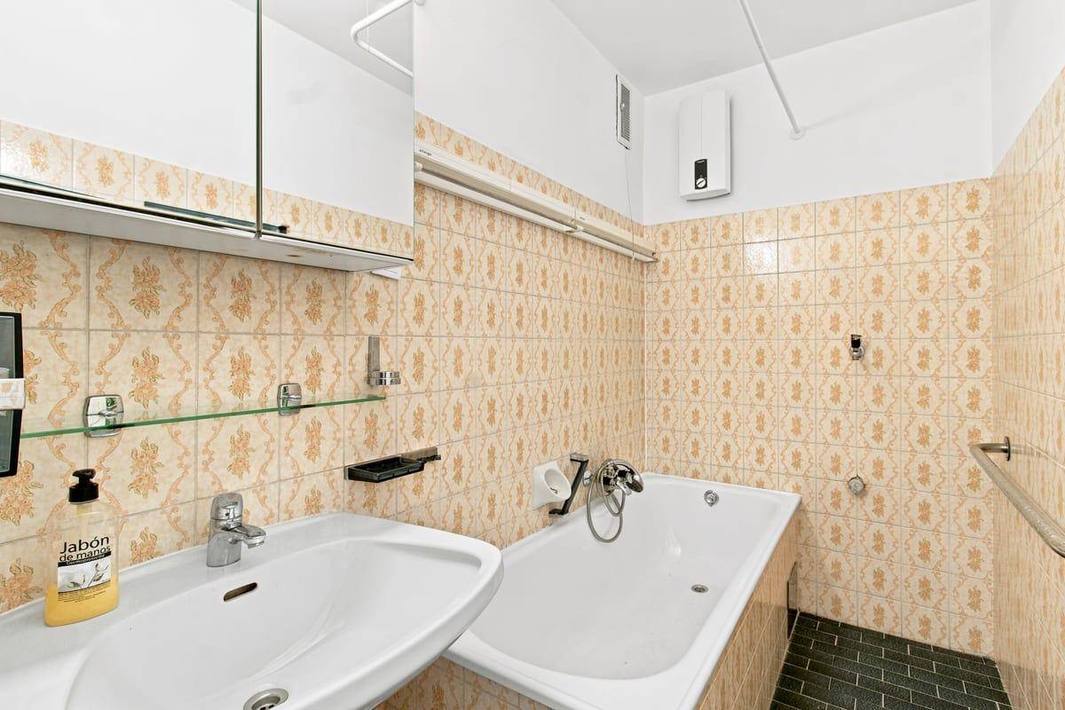 Badezimmer mit Badewanne, Waschbecken und gemusterten Fliesen im Retro-Stil.
